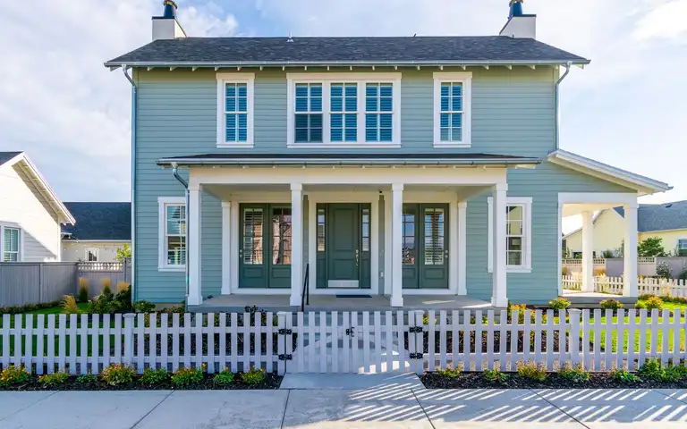 A two-story house behind a white picket fence and gate, with wood privacy fences between neighboring yards